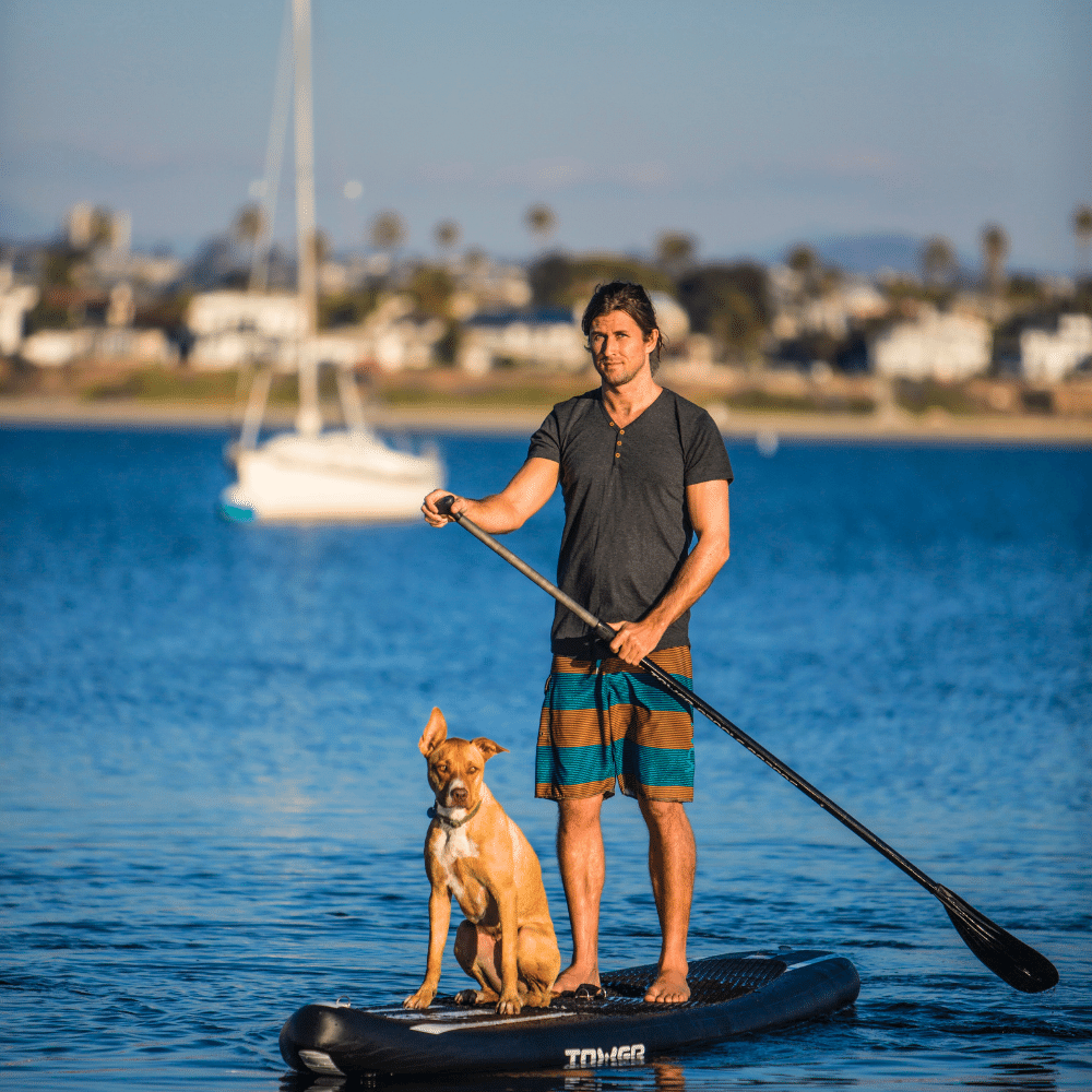 A man happily paddling on a kayak during an outdoor activities for dogs session on the lake.